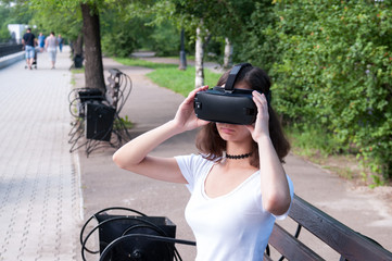 Brunette girl in white t-shirt in Park plays virtual reality in glasses for virtual reality in summer