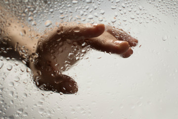 Fototapeta premium hand of a young woman behind glass with water drops on it reaching out