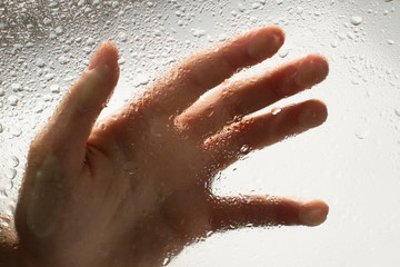 Fototapeta premium hand of a young woman behind glass with water drops on it reaching out