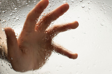 hand of a young woman behind glass with water drops on it reaching out