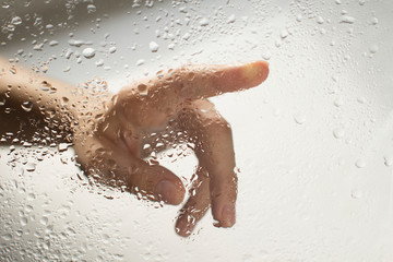 hand of a young woman behind glass with water drops on it reaching out