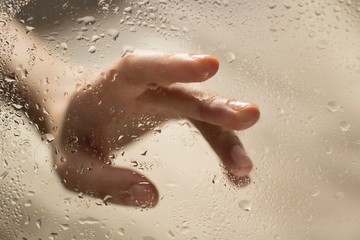 Fototapeta premium hand of a young woman behind glass with water drops on it reaching out