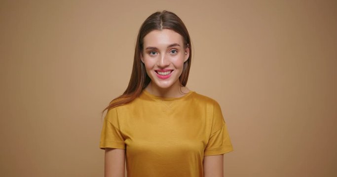Brunette woman in yellow t shirt happy laughs lookong at camera isolated on beige background.