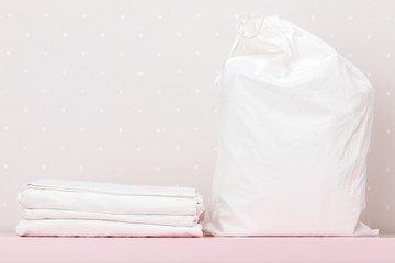 A stack of clean bedding and a storage bag on a white wall background