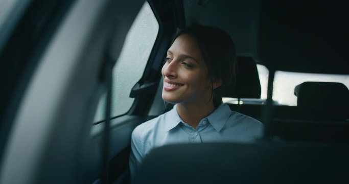 An young businesswoman is looking outside through a window during traveling in a modern car with a driver while is raining outside.