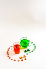 Two fruit carbonated drinks green and red in glass mugs surrounded by colored glass on a white...