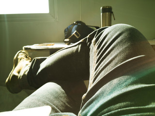 man is leaning back with legs crossed in room, rest at container in morning time, man going to take it easy, photo is yellow filter