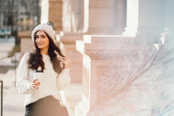 Fototapeta premium Elegant girl standing in a winter city. Woman in a white knited sweater. Beautiful lady with dark hair.