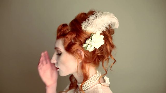 Young vampire woman with long curly hair, pale skin in a white dress on a black background. A beautiful redhead model with red lips. Outfit for halloween. Vampire with open mouth and fangs