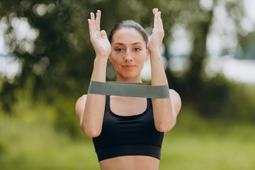 Woman doing exercise for her hands with a tape in the park outdoor. - Image
