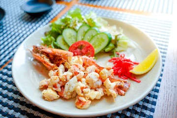 Close up grilled Tiger shrimp with pepper in Japanese style,Cucumber and other vegetable mix salad sesame dressing,lamon and tomato  on side dish.The prawns is sliced and serve on wooden table.