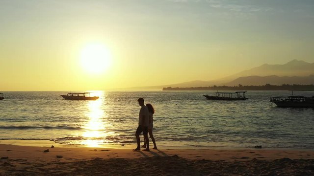 Playful young couple walking around exotic beach on a quiet evening with sun setting down sea horizon reflecting over lagoon full of boats in Jamaica
