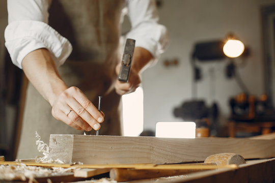 Man working with a wood. Carpenter in a white shirt. Man hammering nails into the wood