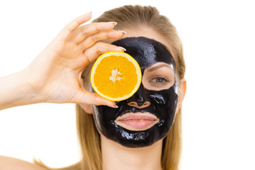 Girl black carbo mask on face holds orange fruit