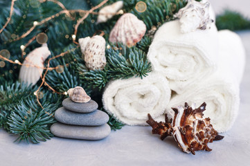 Fototapeta na wymiar Christmas and new year card with fir branches decorated with balls, lights, shells and stones for Spa treatments on a gray background