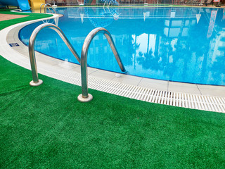Grab bars ladder of swimming pool and green carpet
