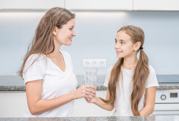 Mom gives daughter a glass of a water at kitchen