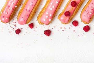 Set of delicious eclairs with pink glaze, raspberry and sugar sprinkles on white background