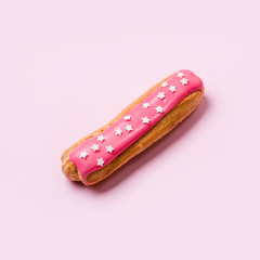 Eclair with pink icing and stars sprinkled on pink background. Food concept