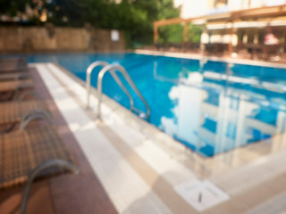 Grab bars ladder of swimming pool and sunbeds around.Blurred and unfocused