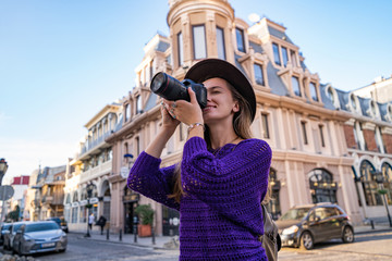 Casual stylish hipster traveler woman photographer in hat with a DSLR camera taking photos during traveling around european city