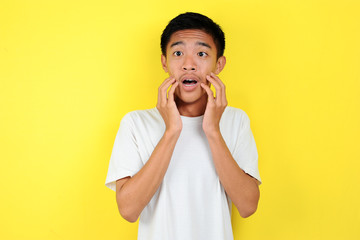 Shocked face of Asian man in white shirt on yellow