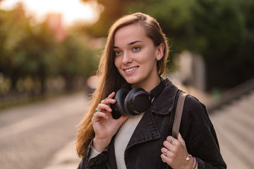 Portrait of stylish fashionable happy joyful hipster student woman teenager with wireless headphones during walking around the city. Music lover enjoying music