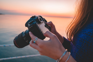 Woman photographer holds dslr camera during taking photos sea at sunset - obrazy, fototapety, plakaty
