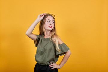 Excited young girl in pastel clothes holding sunglasses under head, keeping hand on glasses isolated on orange background. People sincere emotions lifestyle.