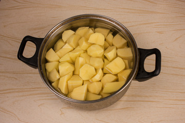 Home kitchen. A pot of peeled and chopped potatoes is on the table