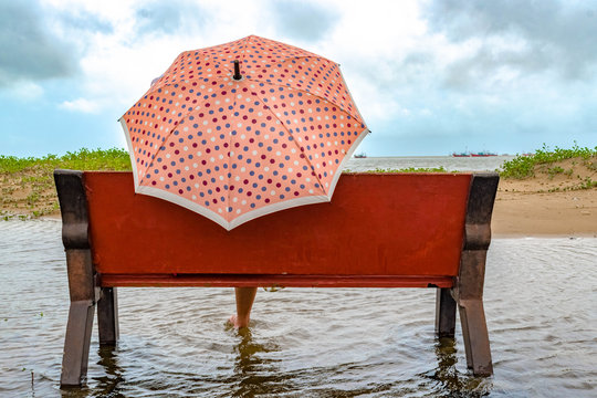 Beautiful Back view of (unrecognizable) girl sitting on beach bench with trendy Umbrella of Polka Dots print. She is relaxed, stress free and having some alone quality time in leisure on a cloudy day.