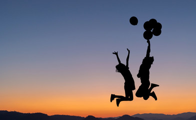 silhouette two children jumping playing on mountain with air balloons at sunset.