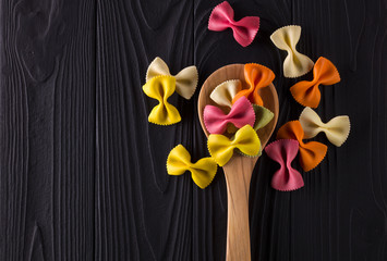 Top view of colorful farfalle pasta on black wooden table with spoon