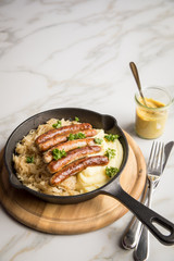 Kleine Bayrische Nürnberger Rostbratwürste mit Sauerkraut, Kartoffelpüree und Senf in rustikaler Gusseisenpfanne auf Holz Brett und Marmor Tisch