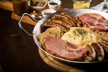 Sauerkraut Pfanne mit Nürnberger Rostbratwürste, Kassler Nacken,  Kartoffelpüree, Senf und Gewürze Zutaten auf Holz Tisch