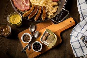 Sauerkraut Pfanne mit Nürnberger Rostbratwürste, Kassler Nacken,  Kartoffelpüree, Senf und Gewürze Zutaten auf Holz Tisch