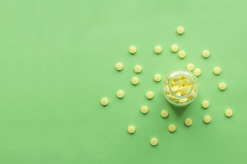 Yellow medical pills scattered from a glass jar on green background with copy space for text. Alternative homeopathy medicine, healthcare and wellness concept. Selective focus