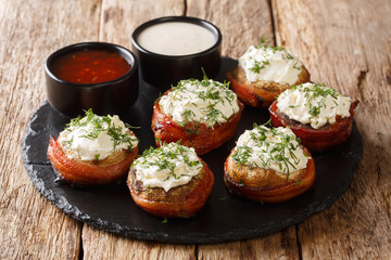 Tasty mushrooms with cream filling wrapped in bacon served with sauces close-up on the table....
