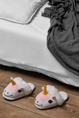 Subject shot of plush house slippers made in the form of white and pink smiling unicorn. The...