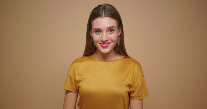 Brunette woman in yellow t shirt happy laughs lookong at camera isolated on beige background.