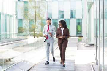 Full length portrait of business partners looking at tablet Full length portrait of business partners looking at tablet. Smiling colleagues walking on street with digital devices. Technology concept