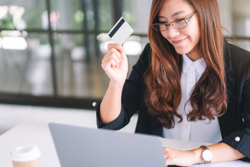 An asian businesswoman holding credit cards while using laptop computer in office