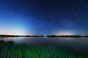 A magical starry night on the river bank with a large tree and a milky way in the sky and falling stars in the summer.