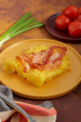 Cheesy potato bake with fried bacon, pickled tomatoes and green onion on yellow plate