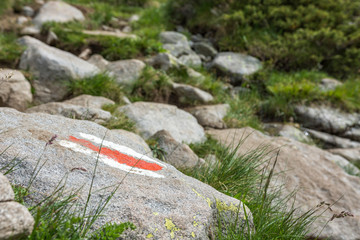 Tourist route mark on stone, painted in white and red guiding the way to Vihren peak, national park Pirin. Beautiful bulgarian mountains. Selective focus. Brook in background.