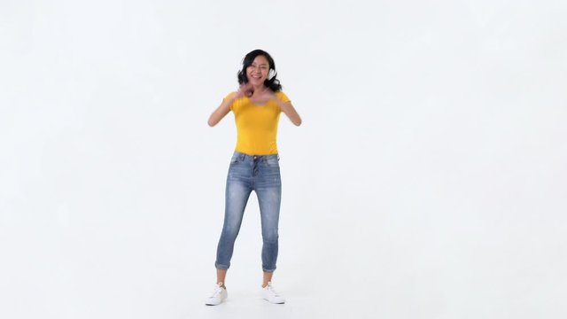 Young happy smiling Asian woman with headphones listening to music and dancing against white background