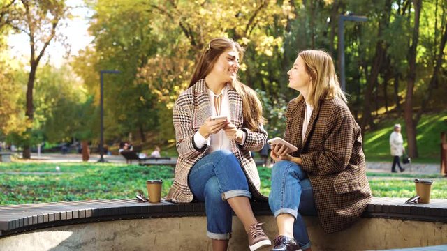 Lovely hipster girls using smartphones in public park on autumn day