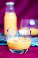 Homemade caramel alcohol drink served in pure glass with ice cubes on concrete tray and blue cloth with purple background