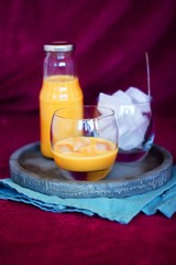 Homemade caramel alcohol drink served in pure glass with ice cubes on concrete tray and blue cloth with purple background