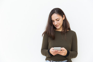 Focused beautiful Latin woman texting message on cellphone. Young woman in casual with mobile phone standing isolated over white background. Digital communication concept